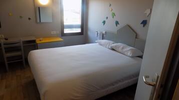 Un dormitorio con cama, escritorio y silla. Se ve un ventanal con vistas al exterior.