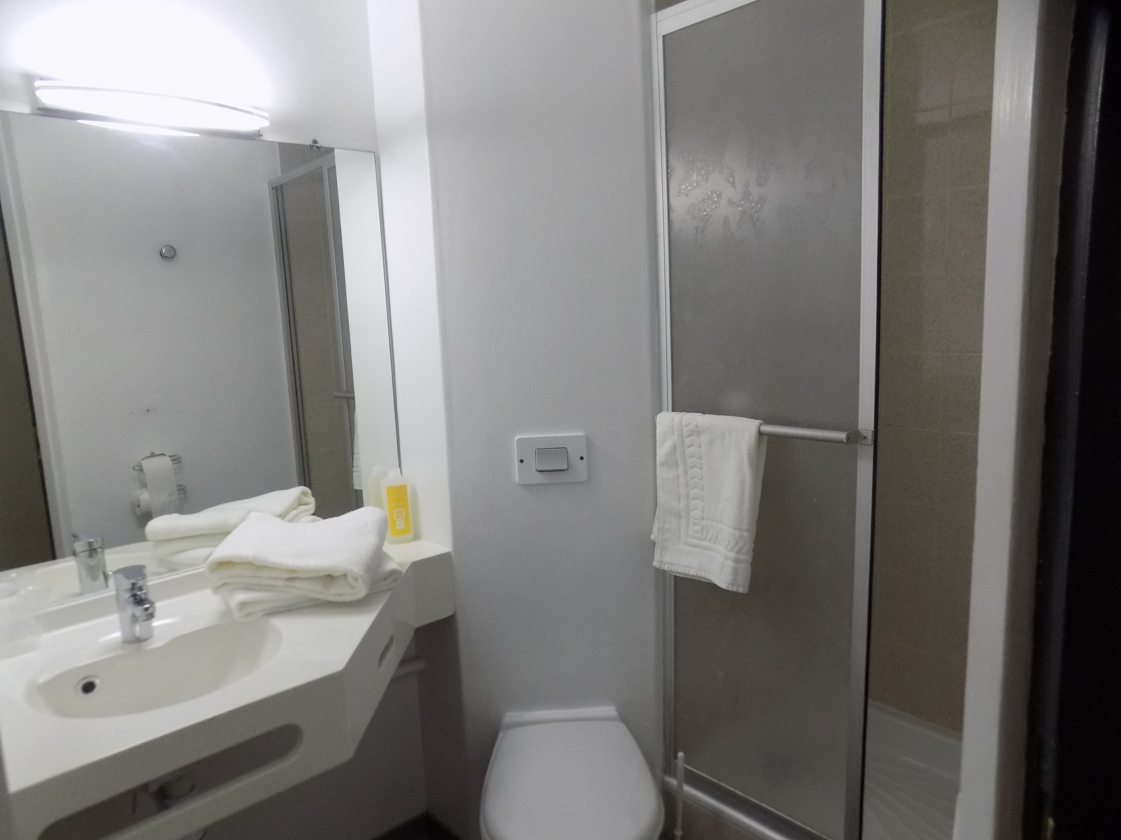 A bathroom with a sink, mirror, toilet, and shower.