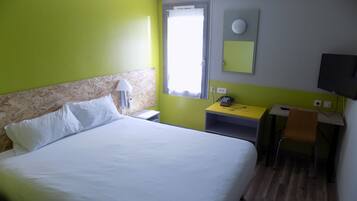 A hotel room with a bed, a desk, a chair, a telephone, and a television.