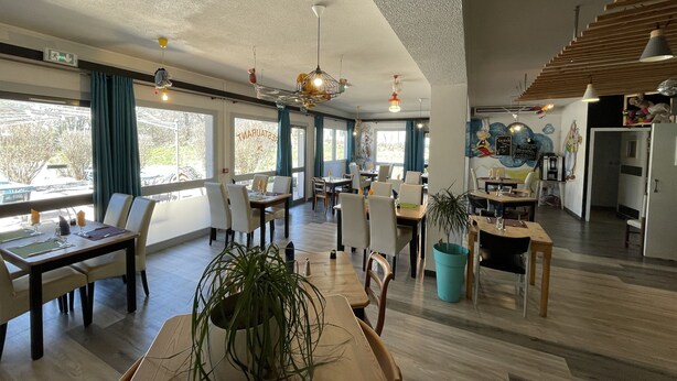 Un vaste espace dédié à la salle à manger, avec de nombreuses tables et chaises, de grandes fenêtres dotées de rideaux et un plafond orné de luminaires suspendus.