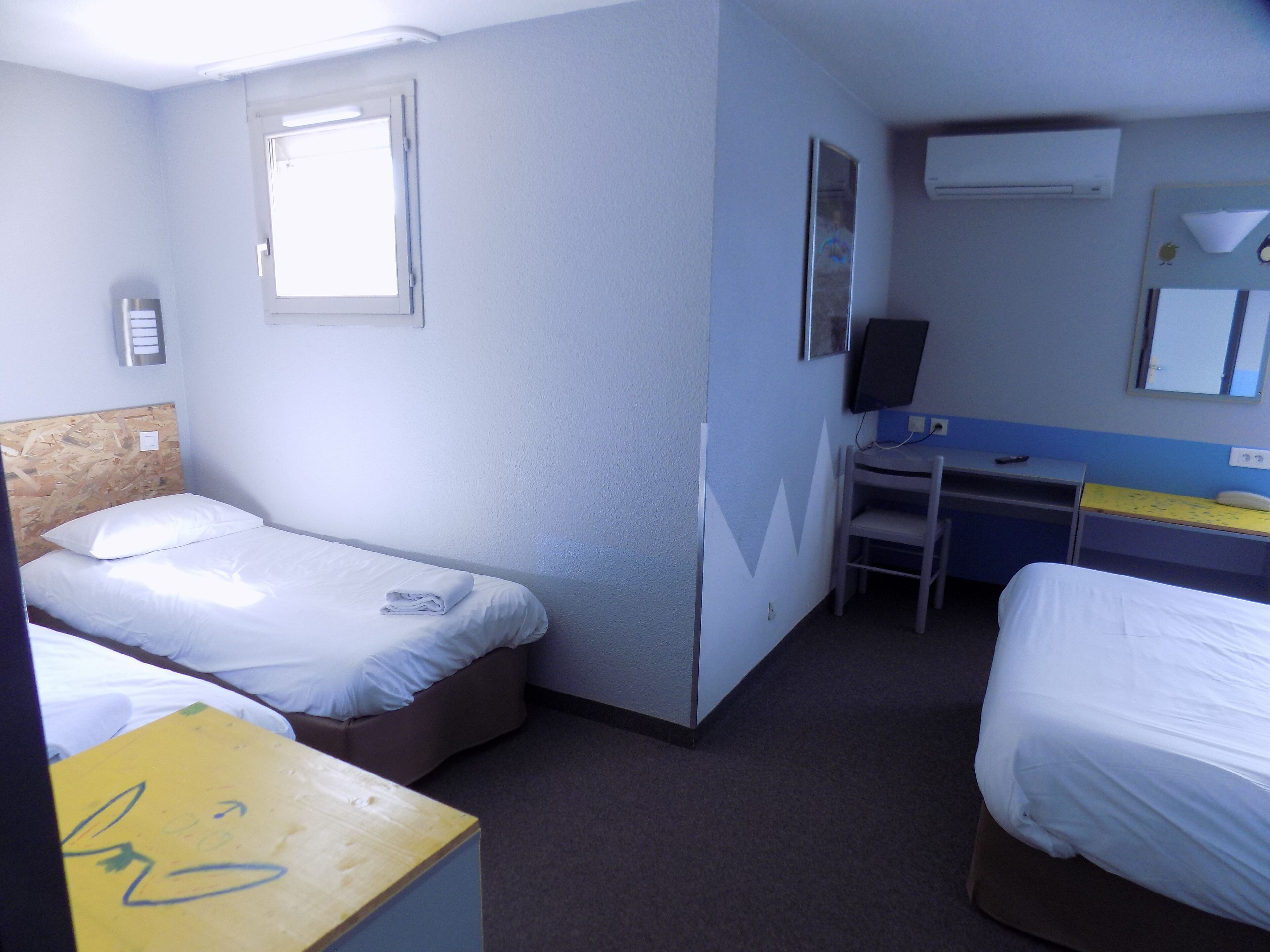 Ein Hotelzimmer mit zwei Betten, einem Schreibtisch, einem Stuhl, einem Fenster und einer Klimaanlage.