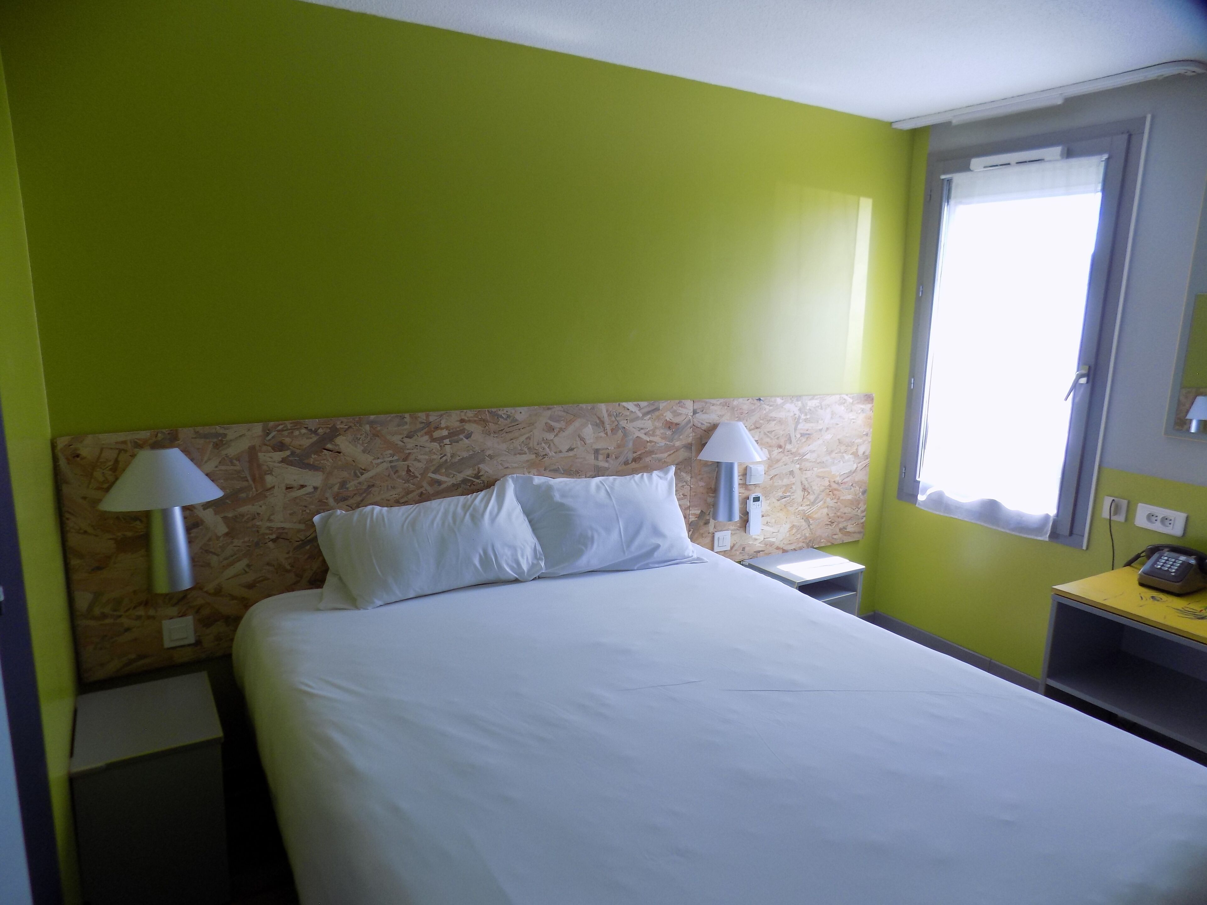 A hotel room with a bed, two bedside lamps, a nightstand, a telephone, and a window with curtains.