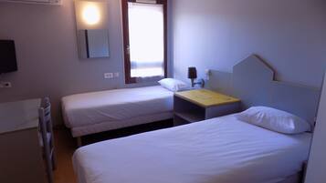 A hotel room with two single beds, a desk, a chair, a TV, and a window with curtains.