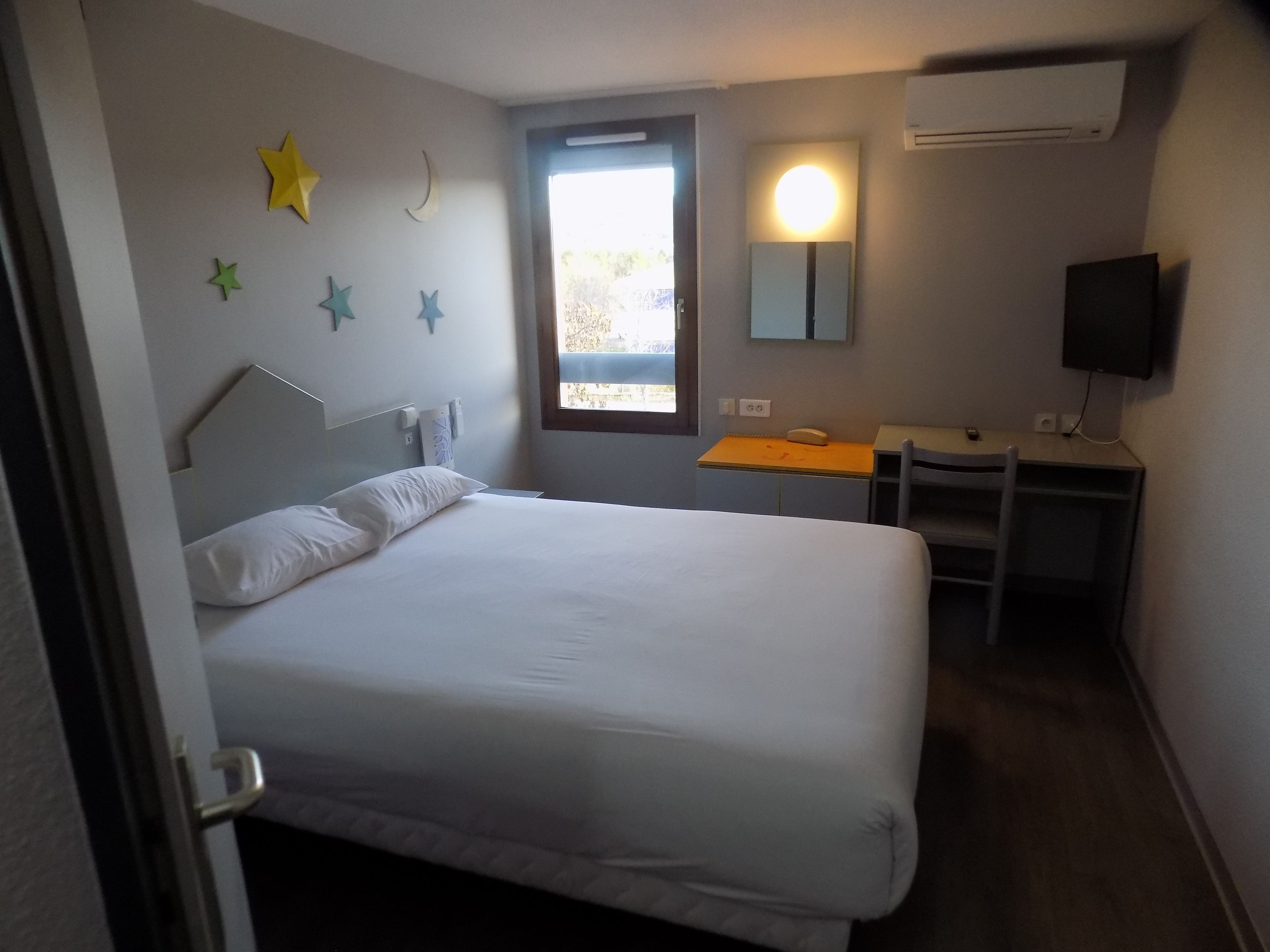 A hotel room with a bed, a desk, a chair, a TV, and a window.