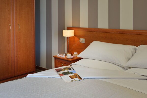 Una cama bien hecha con sábanas blancas, una mesita de noche con una lámpara y una revista sobre la cama.