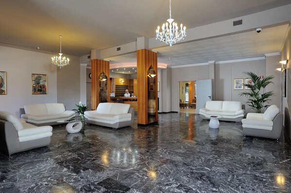 Eine großzügige Lobby mit Marmorboden, weißen Ledersofas und einer prunkvollen Chandelier.