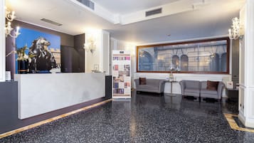 Un hall d’entrée avec un comptoir de réception, une grande fenêtre donnant sur des immeubles, un canapé et une petite table sur laquelle est posé un vase.