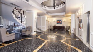 A spacious lobby with a grand staircase, a central seating area, and a modern chandelier.