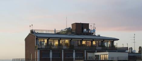 A multi-story building with large windows, a balcony, and satellite dishes on the roof.