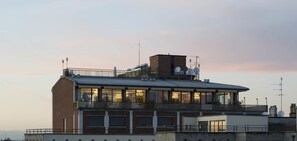 Un edificio a più piani con ampie finestre, un balcone e antenne satellitari sul tetto.
