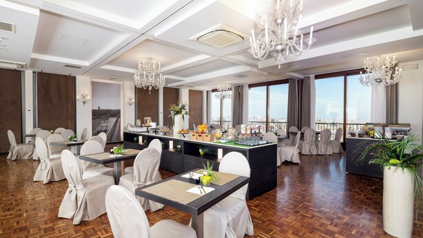 A spacious dining area with high ceilings, chandeliers, and a view of the city.
