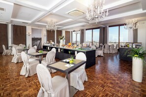 A spacious dining area with high ceilings, chandeliers, and a view of the city.