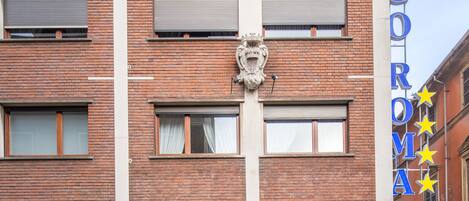 A hotel with a brick facade, a prominent sign reading "GRANDE ALBERGO ROMA", and a large emblem above the entrance.