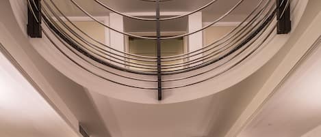 Una majestuosa escalera curva con un candelabro, un área de descanso con un cuadro y un suelo pulido.
