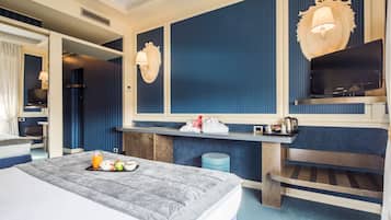 Quarto de hotel com cama, escrivaninha, televisão e banheiro visível por uma porta aberta.