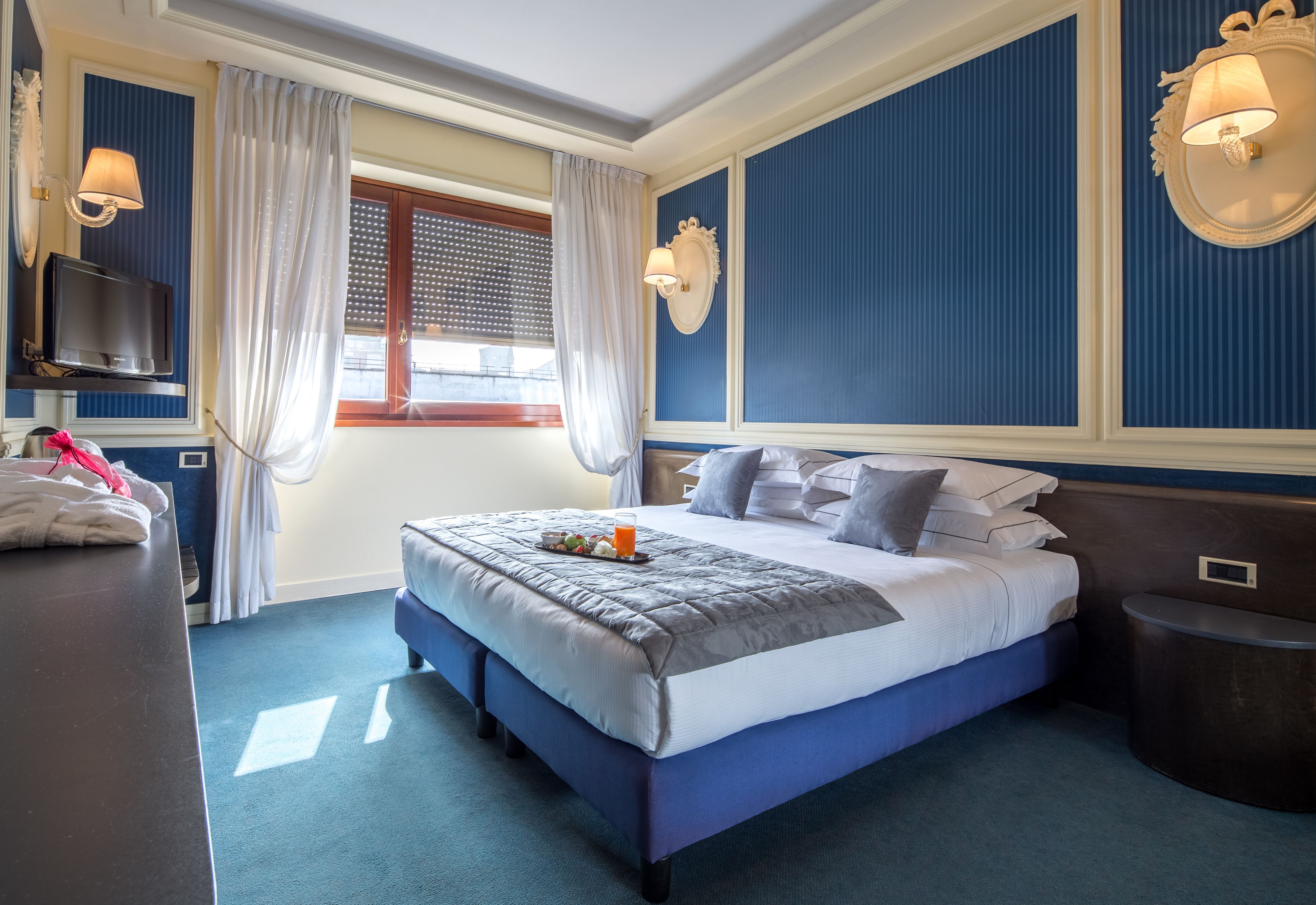 Ein Hotelzimmer mit einem großen Bett, einem Fernseher auf einem Schrank, einem Nachttisch und einem Fenster mit Vorhängen.
