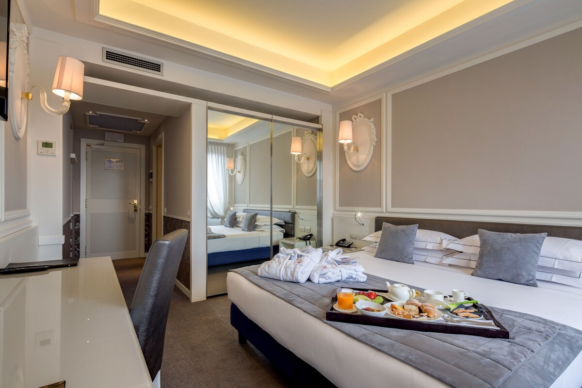 A hotel room with a bed, bedside table, and a tray of breakfast items.