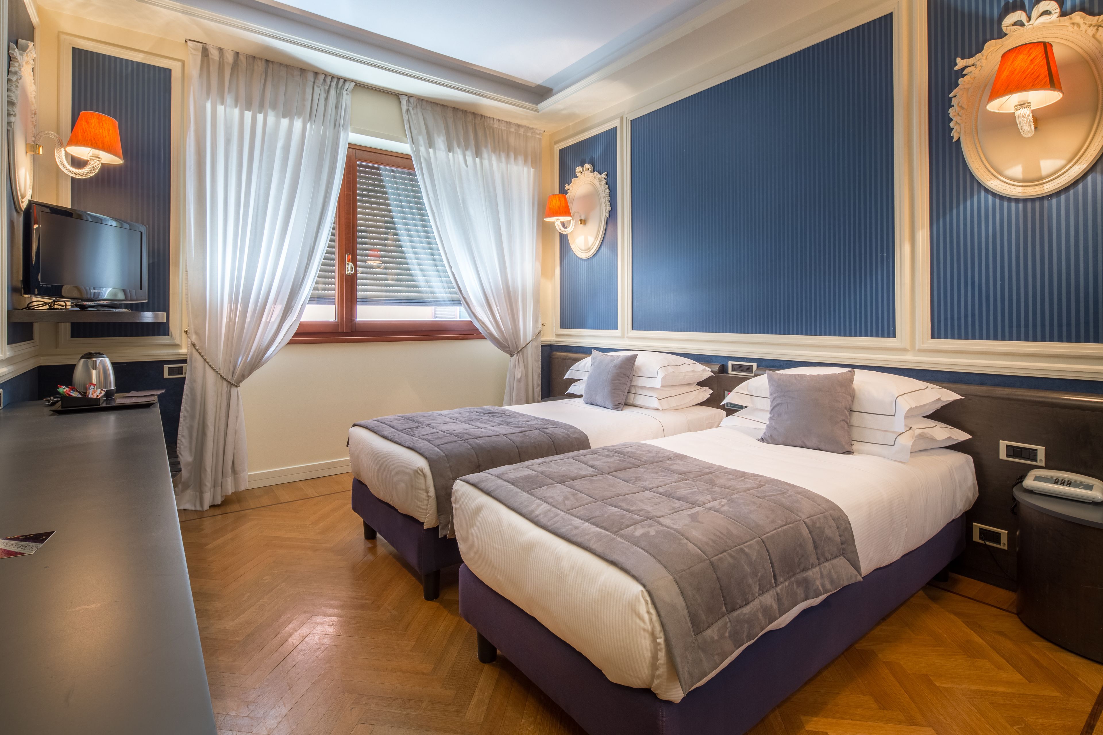 A hotel room with two beds, a TV, a desk, and a window with curtains.