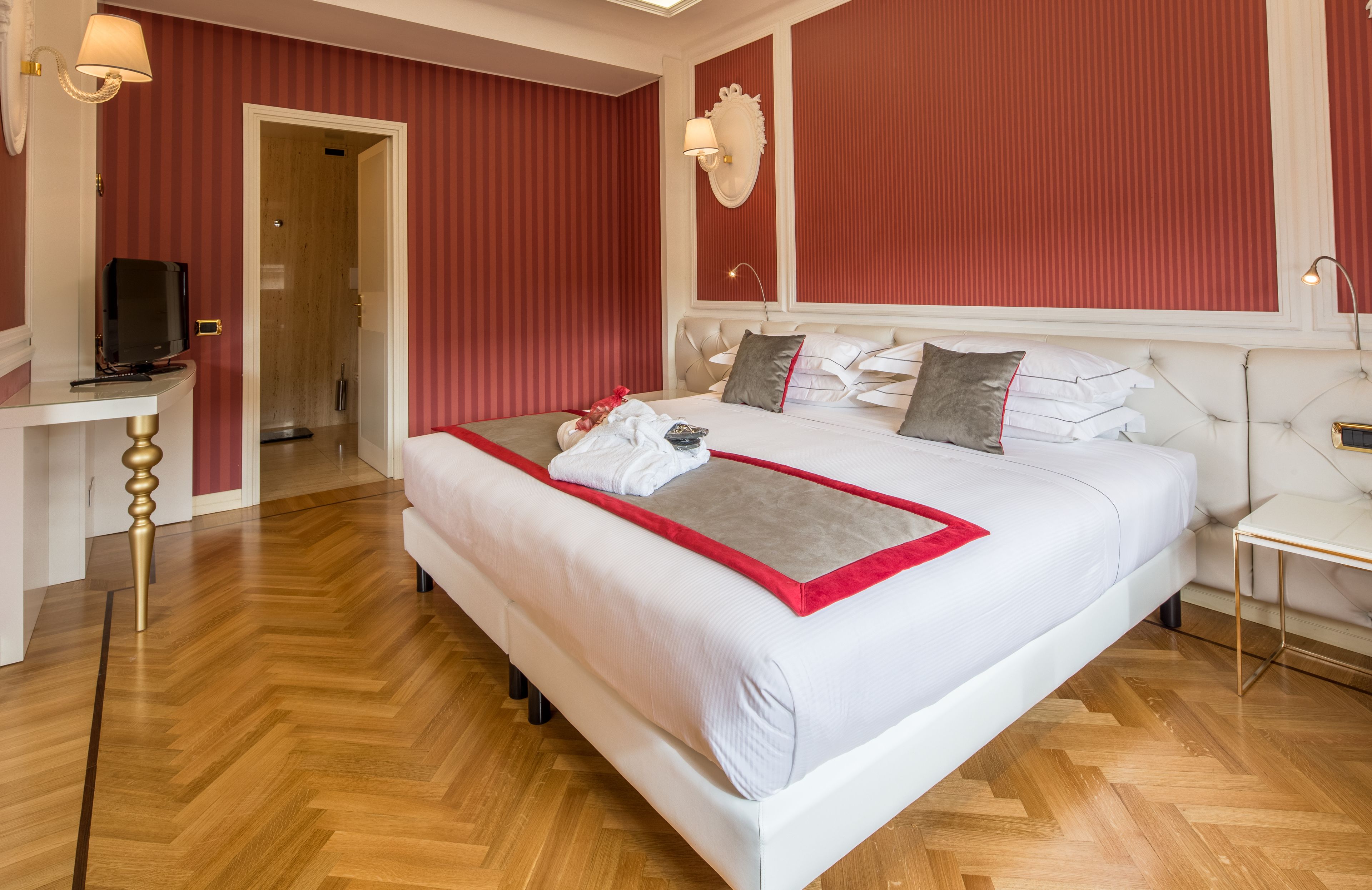 Quarto de hotel com uma cama grande, mesa de cabeceira, televisão e espelho.