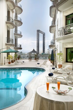 A rooftop pool area with lounge chairs, a table with drinks, and potted plants. - Al Waleed Holiday Homes (Dubai)