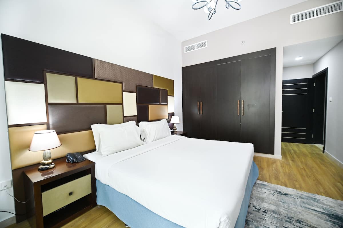 A hotel room with a large bed, a nightstand with a lamp, a telephone, and a wardrobe.