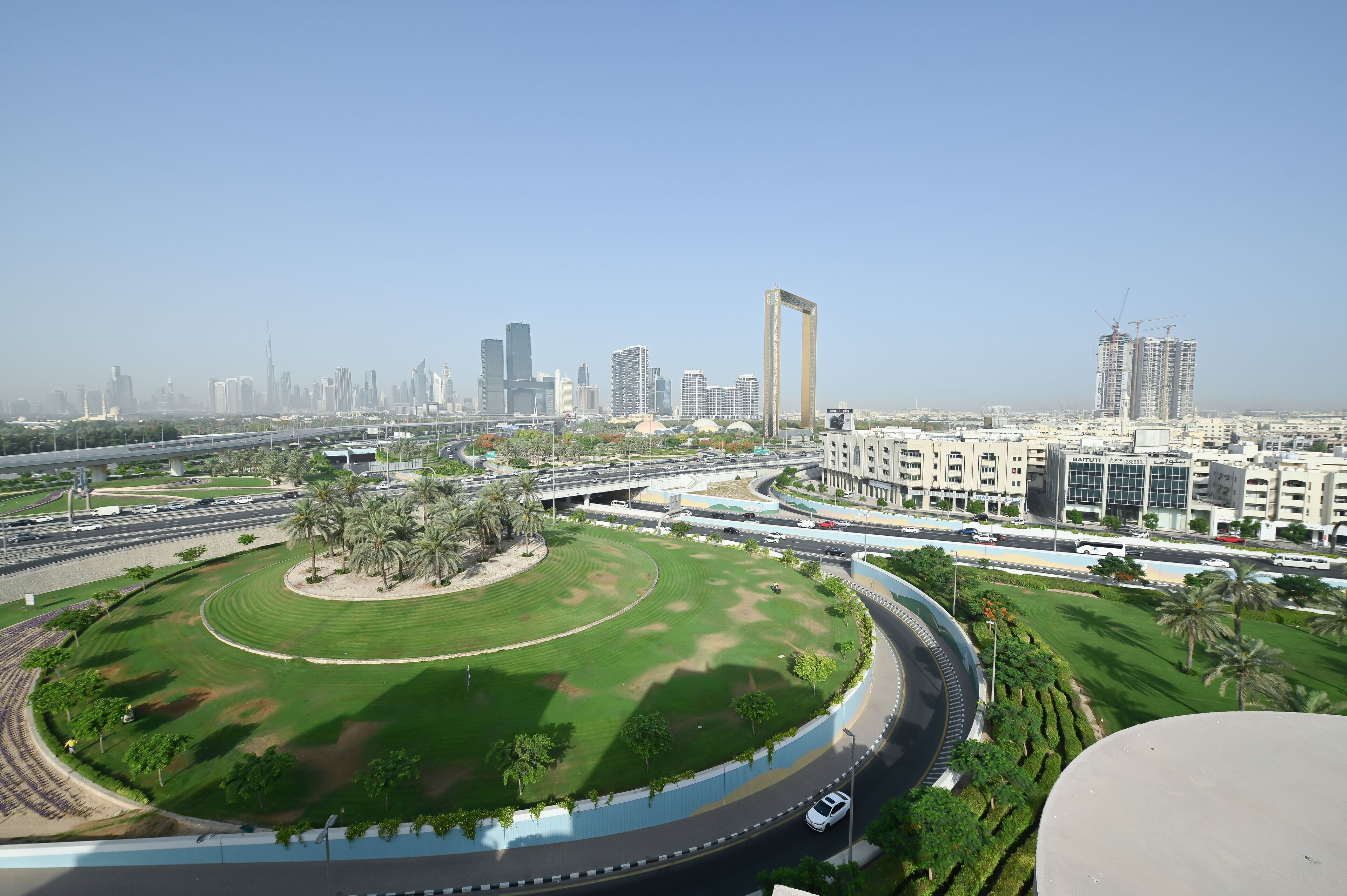 A cityscape with a large circular park, modern buildings, and a highway.