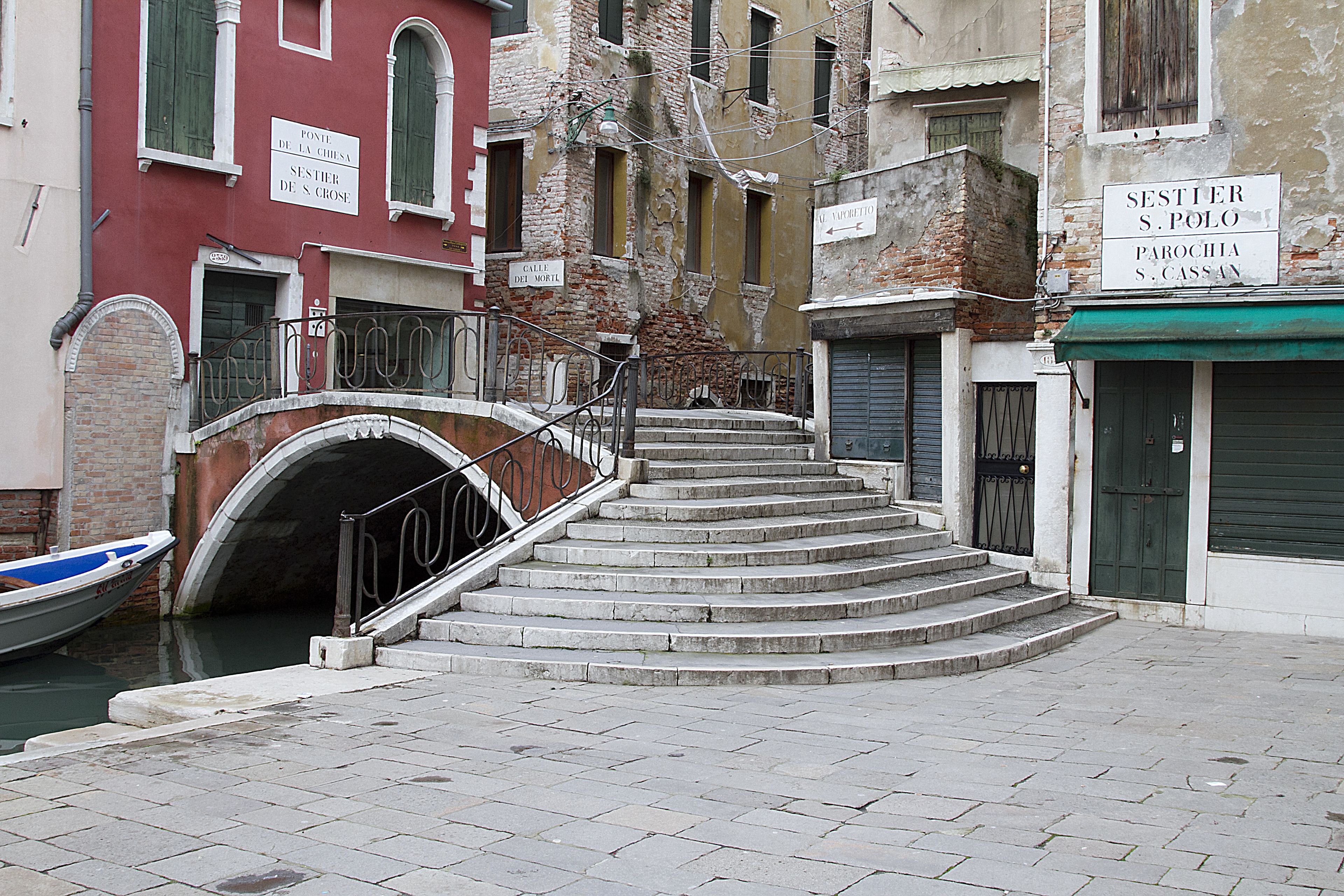 Un estrecho canal veneciano con un puente que lleva a una escalera.