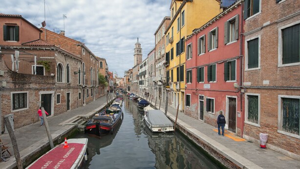 Un canal étroit dans une ville européenne historique, avec des bateaux amarrés le long de ses rives.