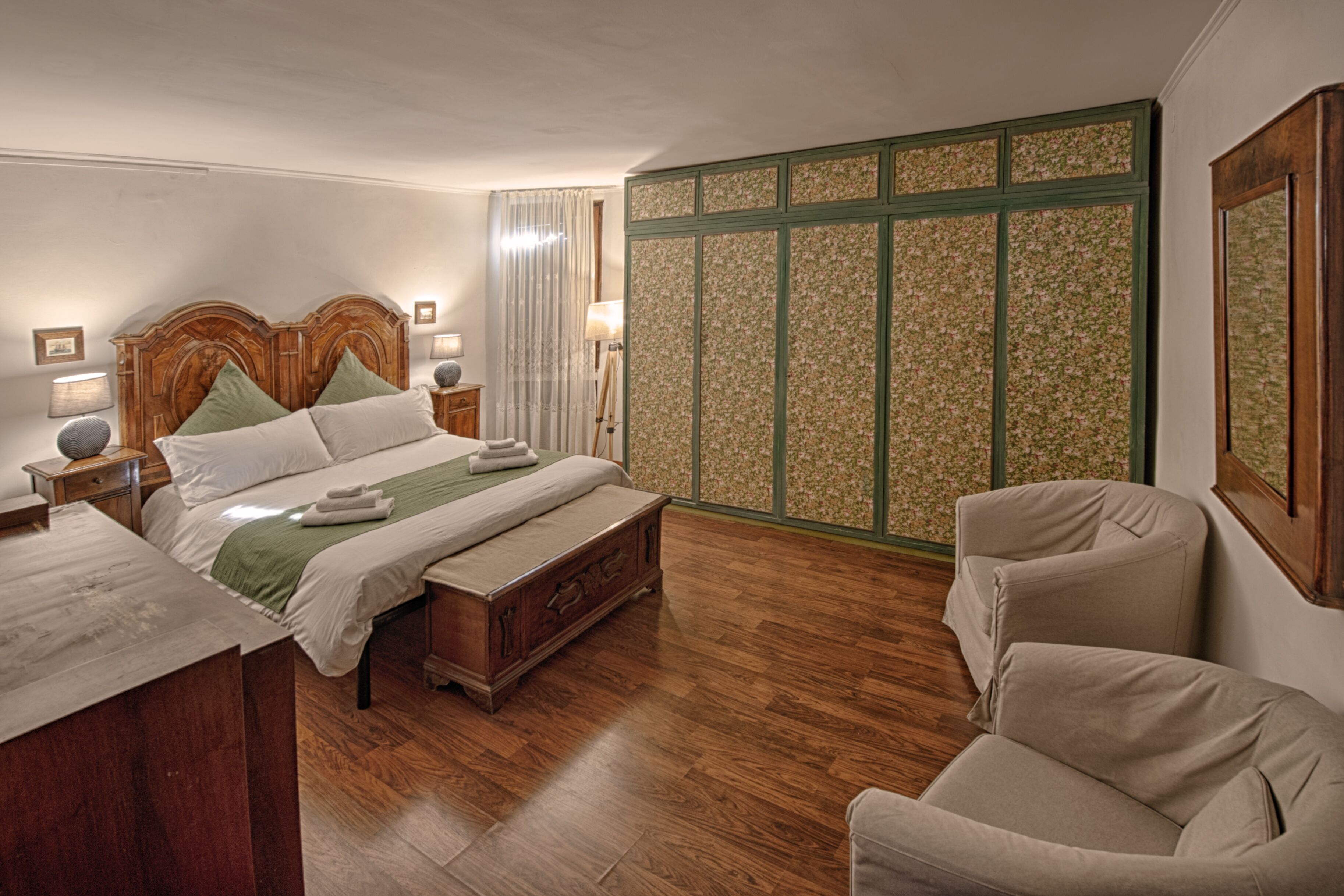 A bedroom with a wooden bed, a nightstand, a chair, and a green patterned wall.