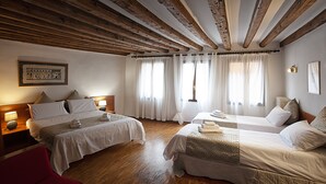 Une chambre d’hôtel avec deux lits, des poutres en bois au plafond et un fauteuil rouge.