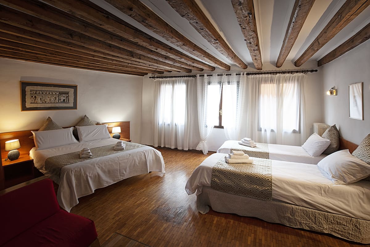 Een hotelkamer met twee bedden, houten balken in het plafond en een rode stoel.