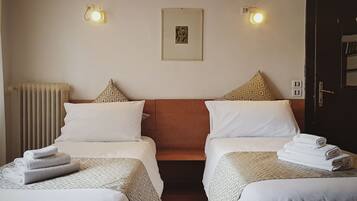 A hotel room with two beds, each with a patterned bedspread, a framed picture on the wall, and two wall-mounted lights.