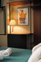 Un letto rifatto con una coperta verde acqua, un quadro appeso sopra e una lampada da tavolo su un comodino.