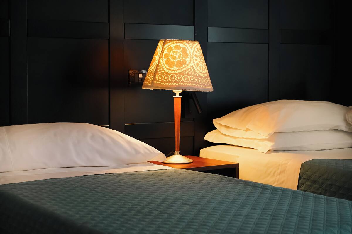 A hotel room with a bed, a nightstand, and a lamp.