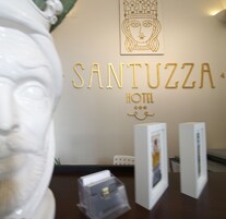 Un muro con il nome 'SANTUZZA HOTEL' e un emblema decorativo sopra. Due quadri incorniciati sono esposti su supporti di fronte al muro.