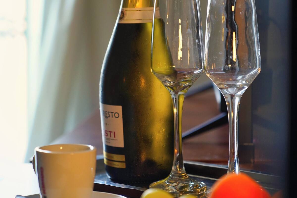 A bottle of wine, two glasses, a cup, and a plate with fruit on a table.
