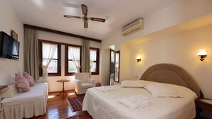 Un dormitorio con una cama, una silla, una mesita, un ventilador de techo y un televisor.