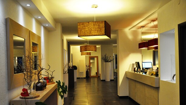 A modern hotel lobby with a long reception desk, multiple pendant lights, and a clean, minimalist design. - Hotel Sandalia (Nuoro)