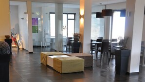 A spacious lobby with a glass coffee table, seating area, and a view of the dining area. - Hotel Sandalia (Nuoro)