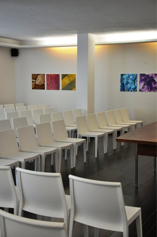 A conference room with rows of white chairs and a long table, with artwork on the walls.