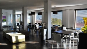 A modern dining area with tables and chairs, large windows with blinds, and a bright vase on the right. - Hotel Sandalia (Nuoro)
