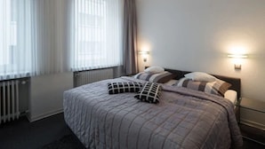 A hotel room with a bed, two bedside lamps, a radiator, and a window with curtains. - Brandenburger Hof (Cologne)