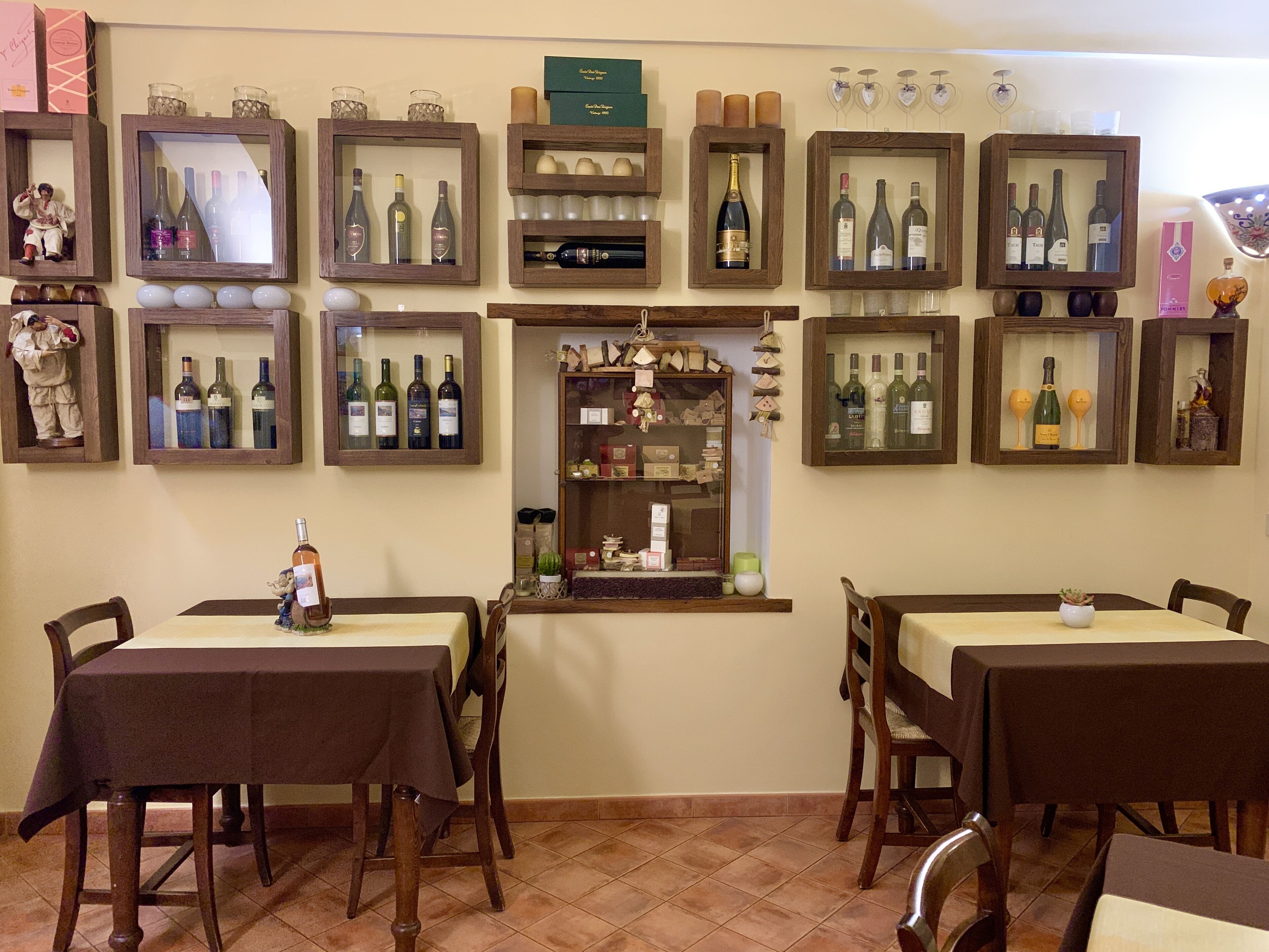 Un ristorante con diversi tavoli e sedie, scaffali in legno che espongono bottiglie di vino e un piccolo bancone con diversi articoli.
