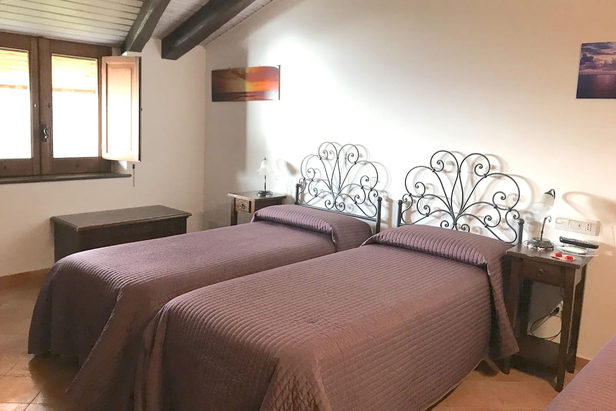 A bedroom with two beds, a wooden bench, a desk, and a wall-mounted lamp.
