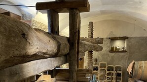 L’intérieur est rustique, avec des poutres en bois, des murs en pierre et un sol dallé. On y trouve des bancs en bois, une cheminée en pierre et des étagères remplies de bouteilles et de pots.