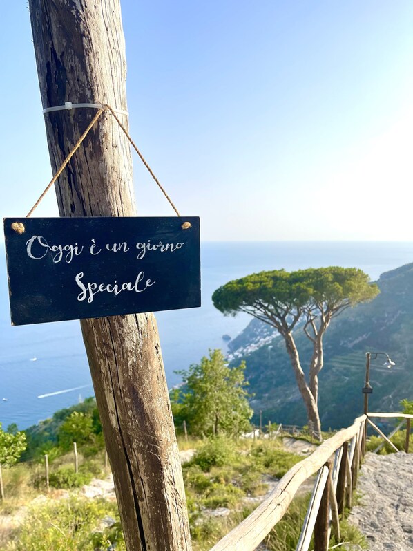 A sign with the text "Oggi è un giorno speciale" hanging on a wooden post with a view of a coastal landscape in the background. - Affittacamere Sant'Alfonso (Furore)