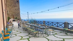 Un espace extérieur aménagé pour les repas, avec des tables et des chaises, un mur en pierre et une vue sur la mer.