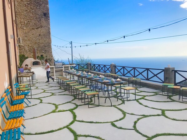 An outdoor dining area with tables and chairs, a stone wall, and a view of the sea. - Affittacamere Sant'Alfonso (Furore)