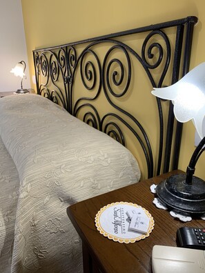 Una cama bien tendida con un cabecero decorativo, una mesita de noche con una lámpara, un control remoto y un mantel individual con un nombre.