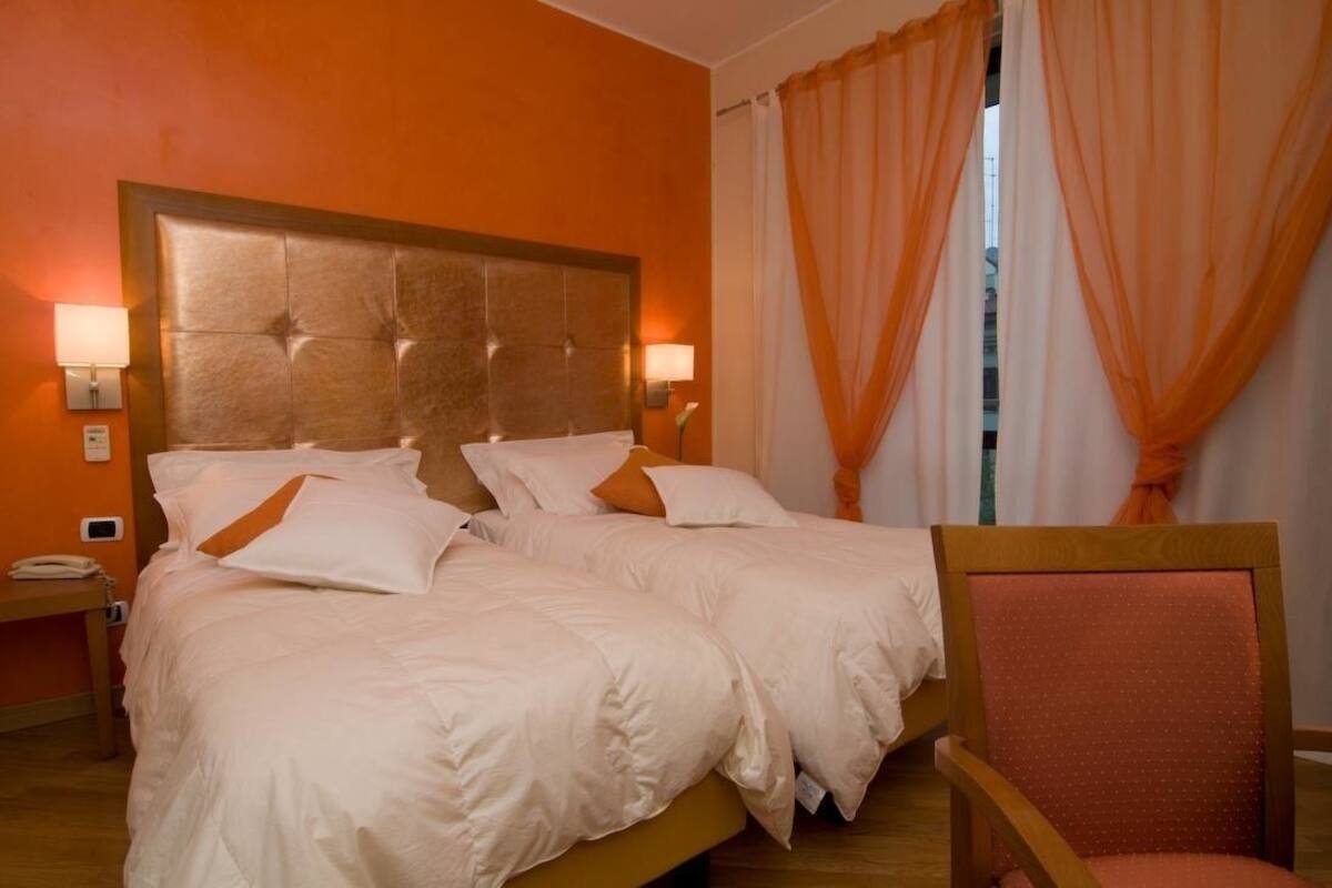 A hotel room with two beds, a wooden headboard, a nightstand with a phone, and a chair.